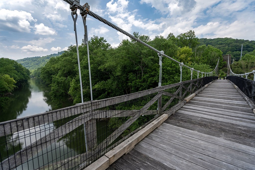 A wooden suspension bridge over a river with green trees on the sides.