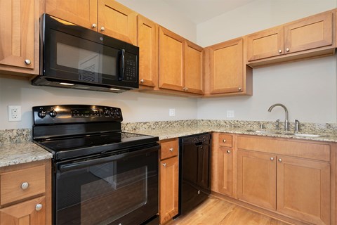 A black microwave oven is mounted above a black stove in a kitchen with wooden cabinets.