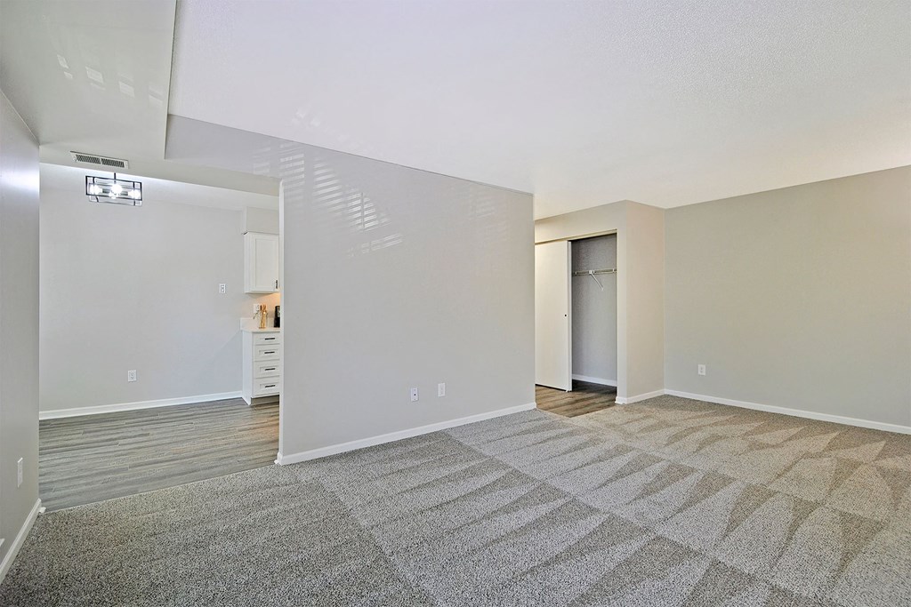 the living room and dining room of an apartment with carpeting and white walls