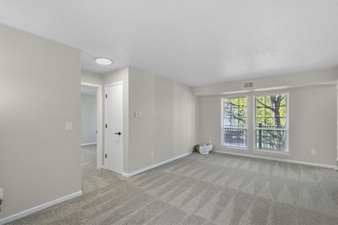 an empty living room with a large window and carpeting
