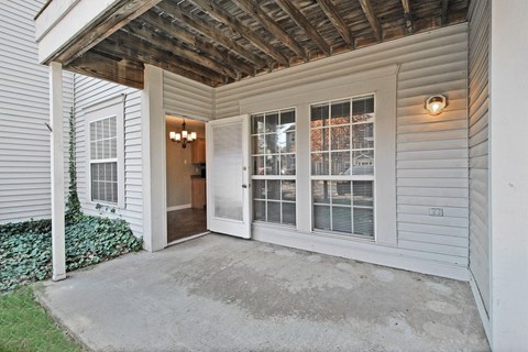 the front porch of a white house with a concrete driveway and a door to a