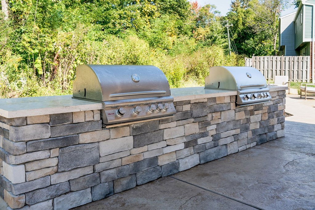 a stone wall with two bbq grills in a backyard