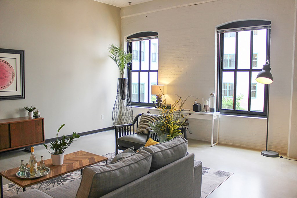 A living room with a grey couch and a coffee table with a vase of flowers on it.