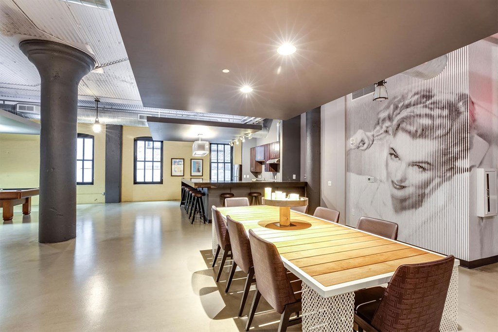 A long wooden table is surrounded by chairs in a room with a large poster on the wall.
