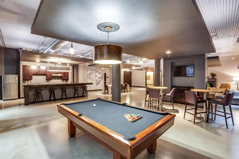 A pool table is in the middle of a room with a bar and a television.