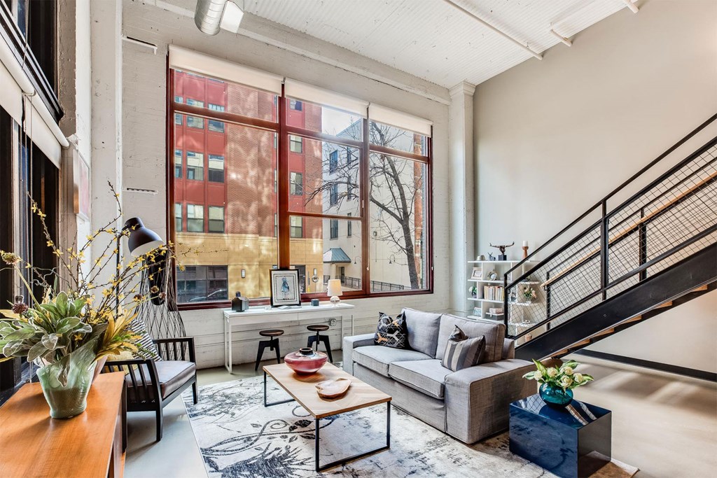A living room with a grey couch, a coffee table, a staircase, and a large window.