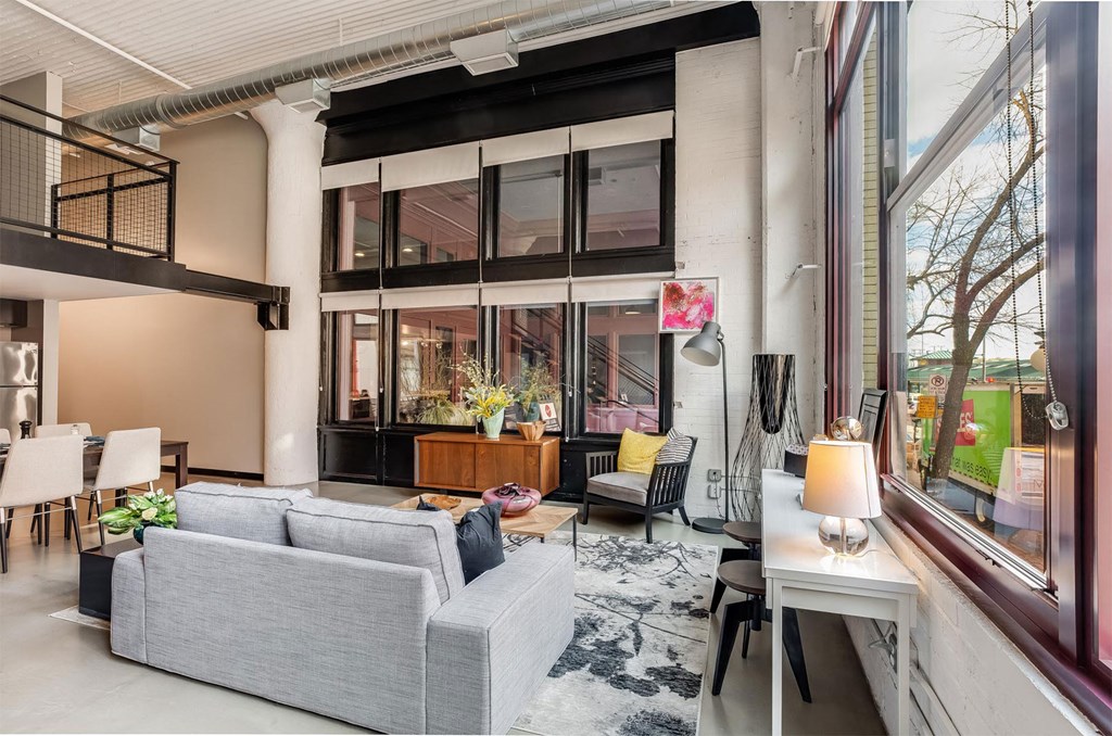 A grey couch sits in a well lit room with a table and chairs.