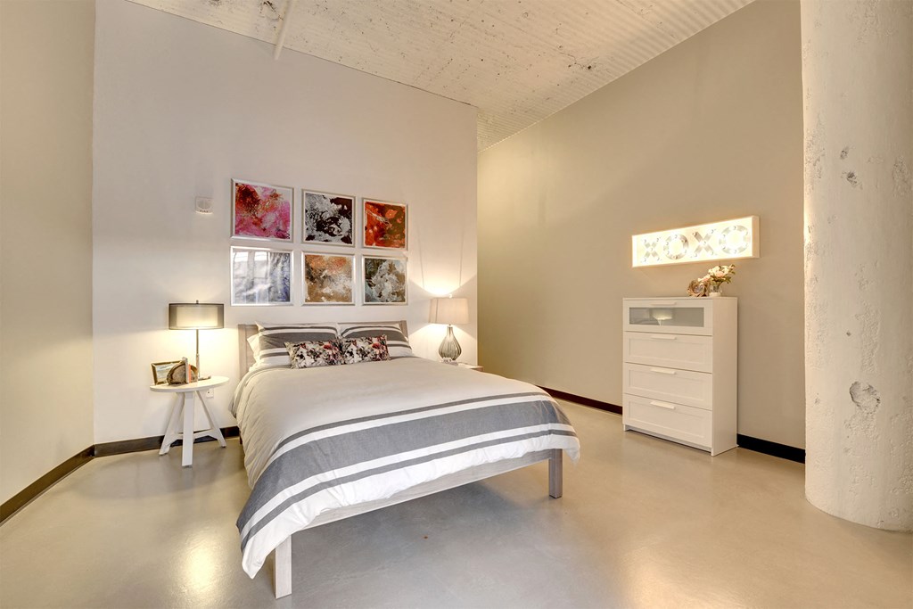 A bedroom with a bed, nightstand, and a white dresser.