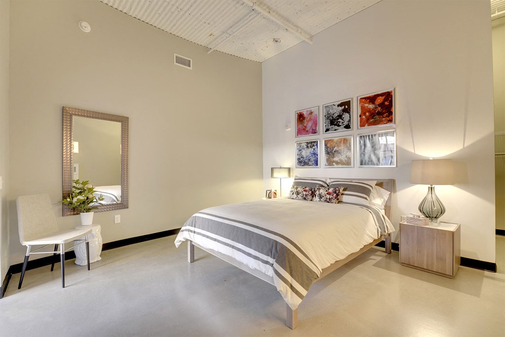 A bedroom with a large bed, a chair, a mirror, and a wall-mounted lamp.