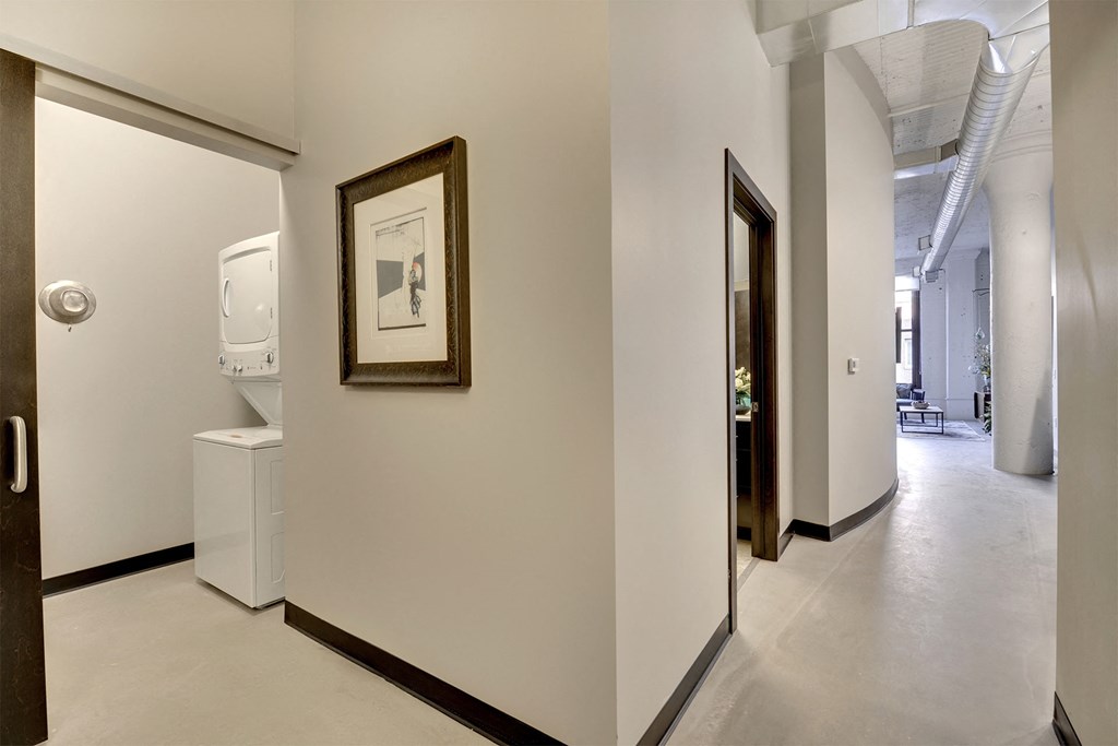 A hallway with a framed picture on the wall and a white trash can.