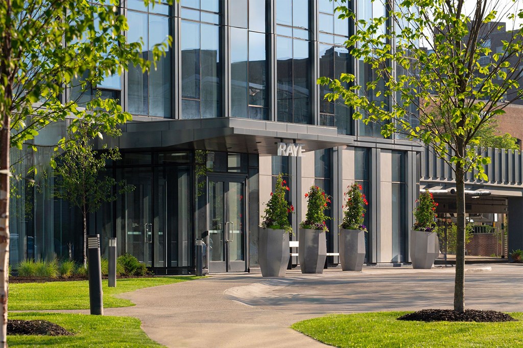 A modern building with glass windows and a sign that reads "RAY" is surrounded by trees and plants.
