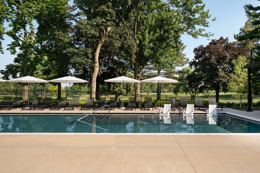 A pool surrounded by trees and chairs with umbrellas.