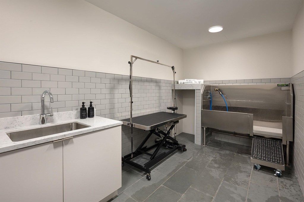A clean, white-tiled kitchen with a sink, stainless steel table, and a walk-in shower.