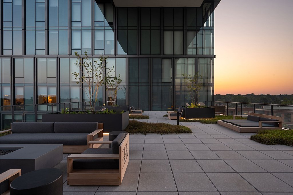 A modern building with a glass facade and a rooftop terrace with seating.