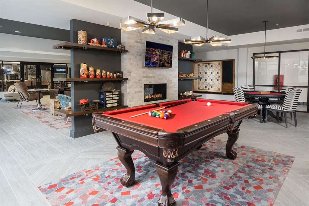 A pool table is in the middle of a room with a fireplace and shelves with various items.