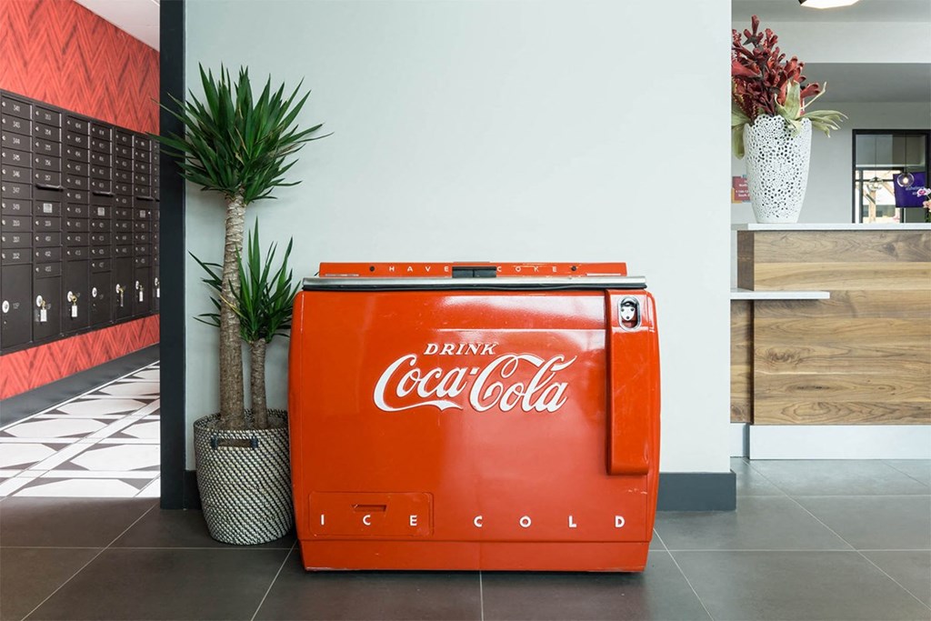 A Coca Cola cooler sits on a tiled floor in a room.
