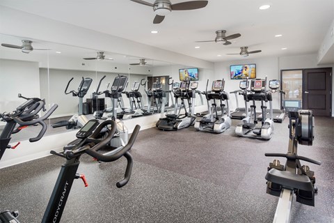A spacious gym with a variety of exercise equipment including treadmills, stationary bikes, and elliptical machines.