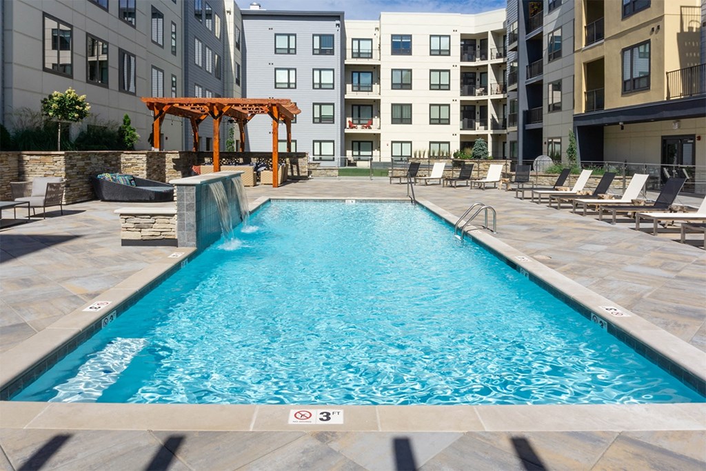 A swimming pool in a residential area with a wooden pergola.