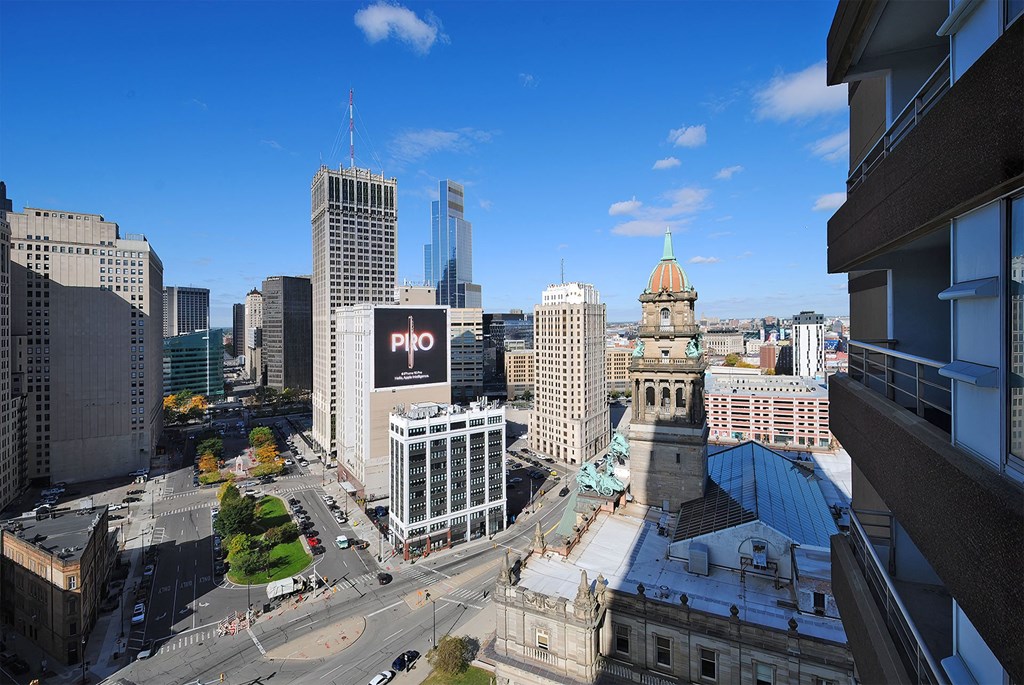 A cityscape with a mix of modern and older buildings, a clear blue sky, and a road with moving vehicles.