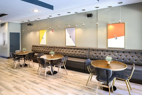A modern dining area with a grey sofa, wooden tables and chairs, and a grey and yellow artwork on the wall.