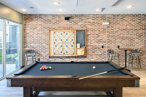 A pool table with a brick wall and a framed picture above it.