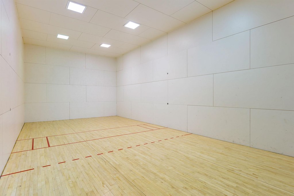 A squash court with wooden flooring and white walls.