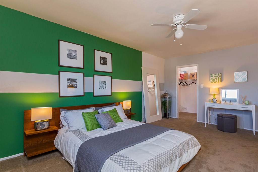 A bedroom with a bed, a desk, and a ceiling fan.
