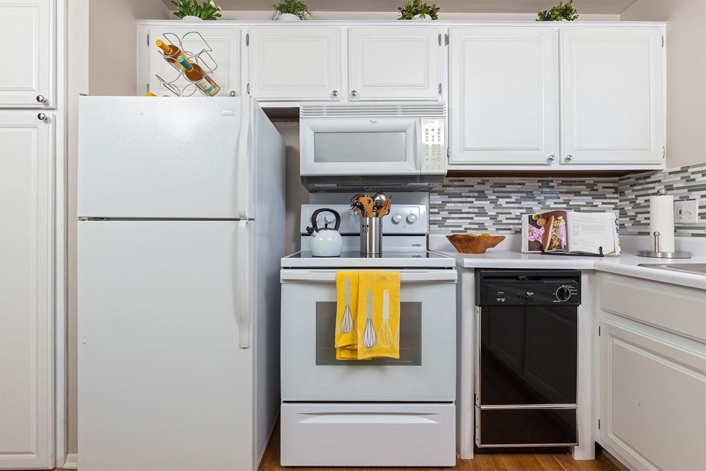 A kitchen with a white refrigerator and a white oven with a yellow towel hanging on it.