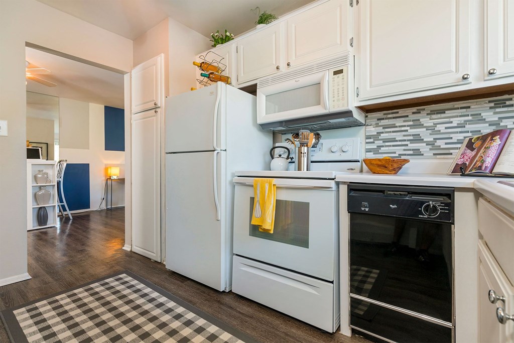 A kitchen with white appliances and a checkered rug.
