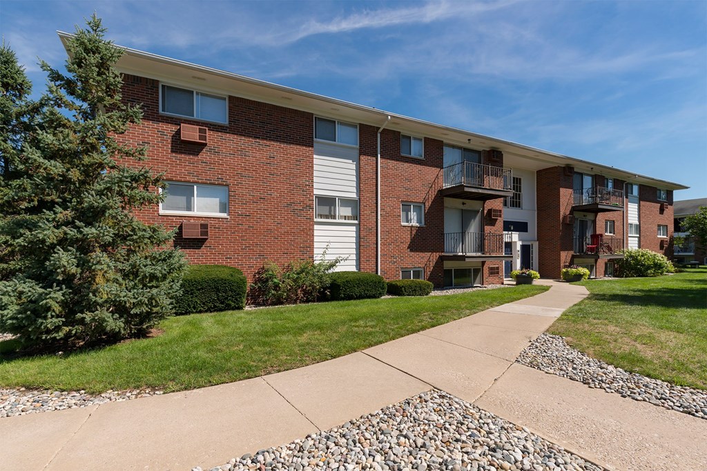 A red brick apartment building with a sidewalk in front.