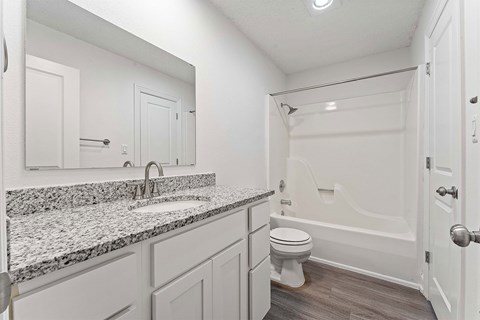 A white bathroom with a marble countertop and a white toilet.