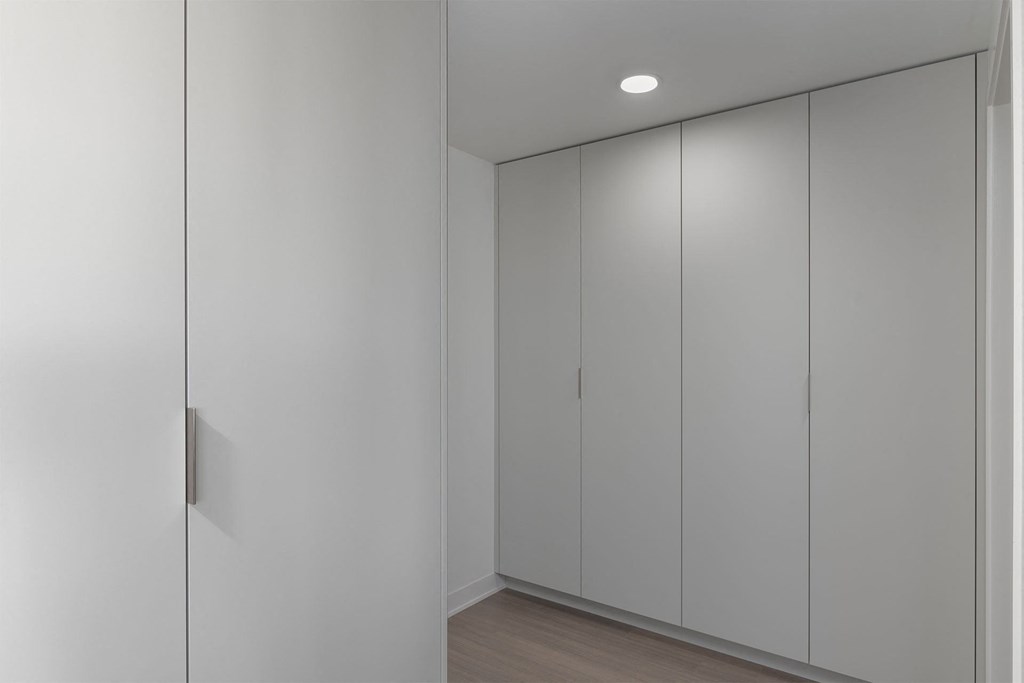 A white hallway with a door on the left and three doors on the right.