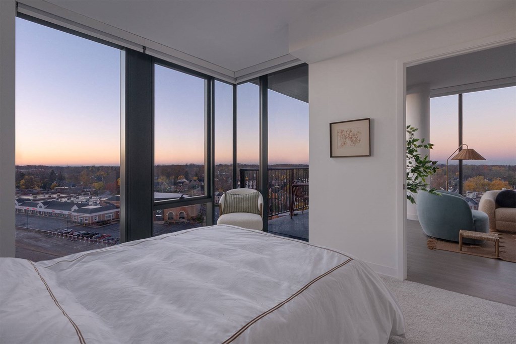 A bedroom with a large bed and a view of the city at dusk.