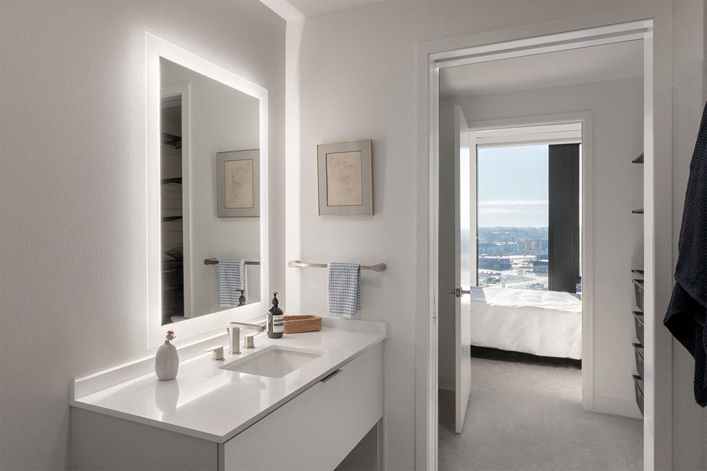 A white bathroom with a large mirror and a window overlooking the city.
