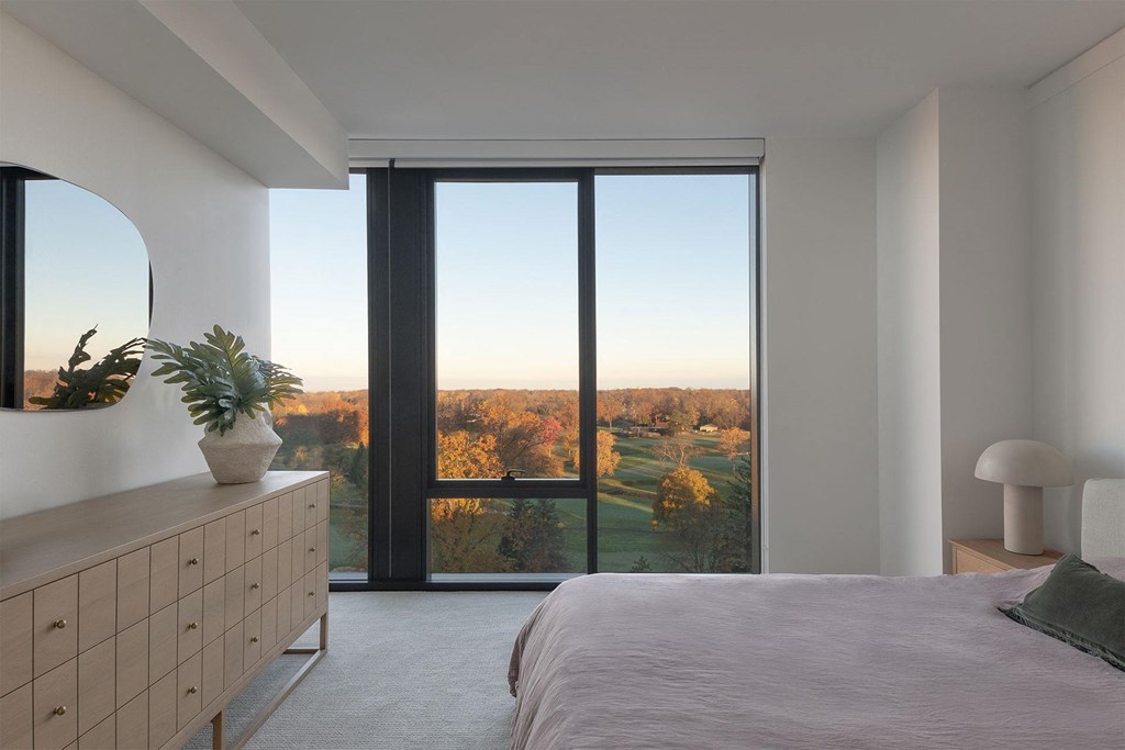 A bedroom with a large bed and a view of the outdoors through a large window.