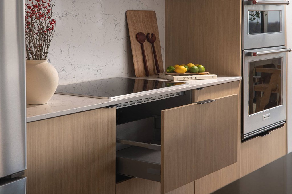 A kitchen with a stainless steel refrigerator, a wooden cutting board, and a bowl of lemons and limes on a counter.