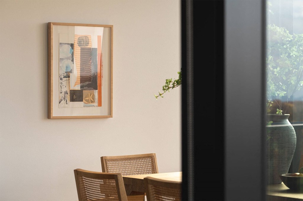 A framed picture hangs on a wall above a table with chairs.