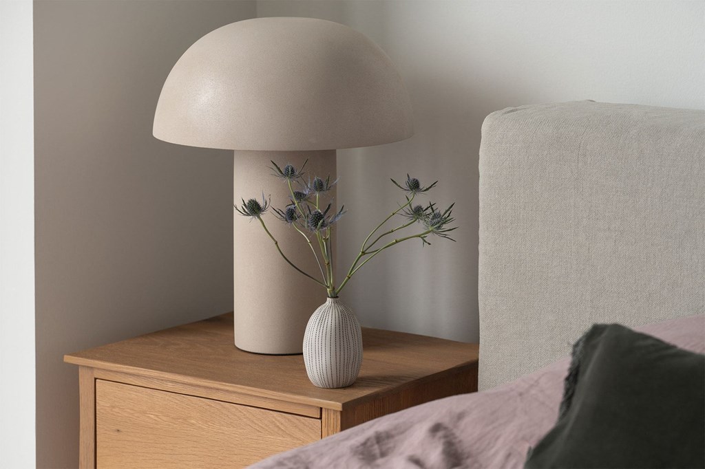 A lamp with a flower arrangement on a nightstand next to a bed.