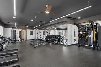 A spacious gym with a variety of equipment including treadmills, weights, and a ceiling fan.
