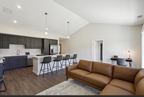 A modern living room with a brown leather couch and a kitchen area with a white counter.
