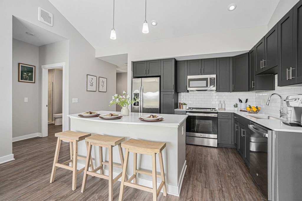 A modern kitchen with a white island and wooden stools.