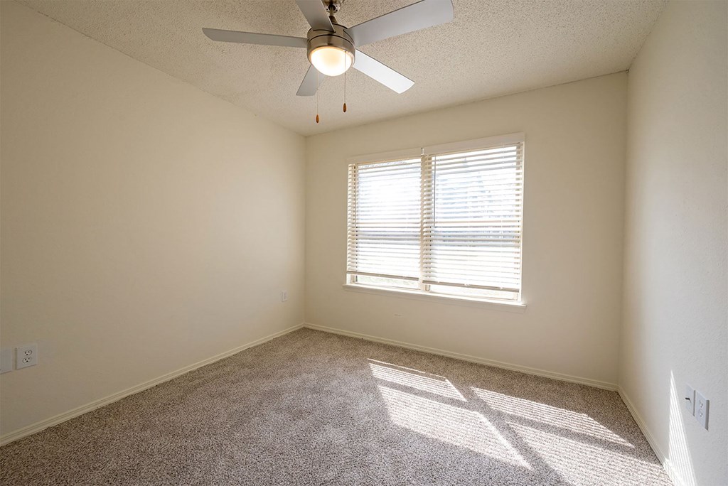 A room with a ceiling fan and a window with blinds.