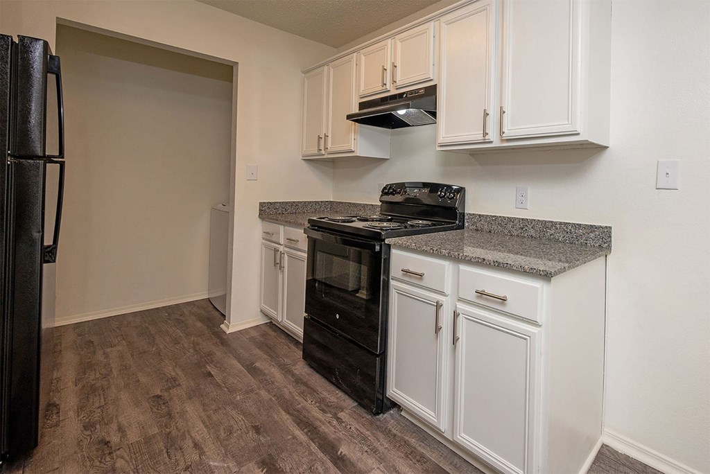 A kitchen with a black fridge, black stove, and white cabinets.
