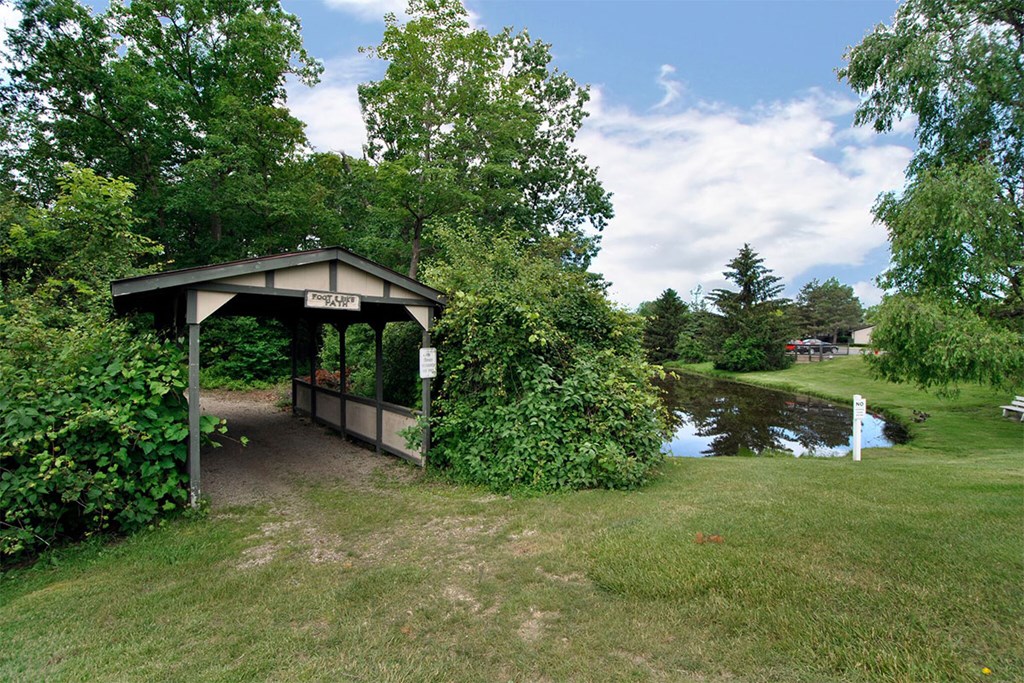 A gazebo is surrounded by greenery and a pond.