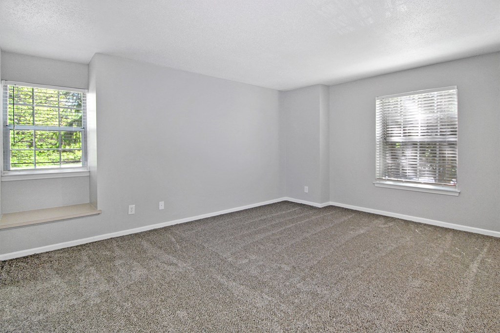 an empty living room with carpet and two windows