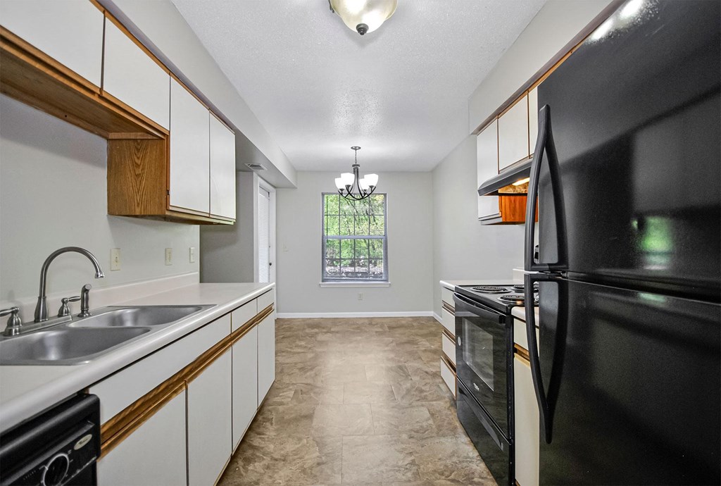 A black refrigerator in a kitchen with white cabinets and a window.