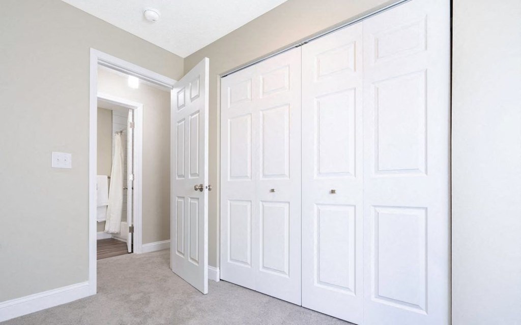 an empty bedroom with white closets and a carpeted floor