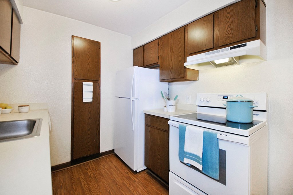 A kitchen with a white refrigerator, white stove, and wooden cabinets.