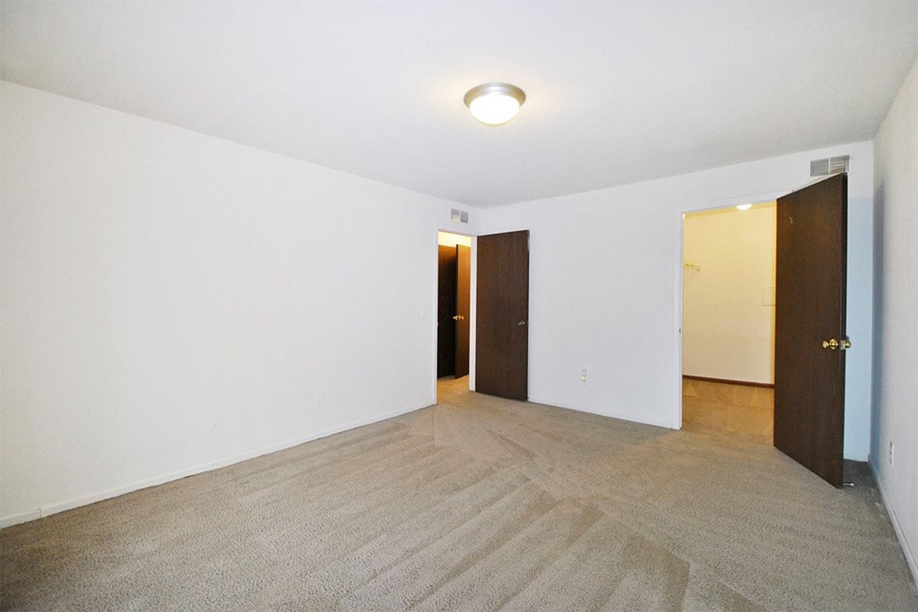A room with carpeted floor and white walls with two doors.
