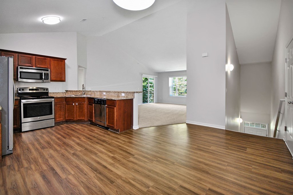 an empty kitchen and living room with wood flooring and stainless steel appliances